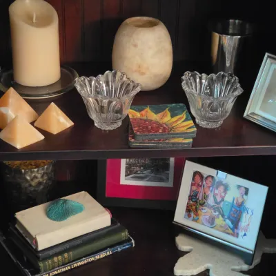 Sale Photo Thumbnail #93: Collection of decorative home accents, including small crystal bowls, alabaster pyramids, candles, framed art, and stacked books on dark wooden shelving.