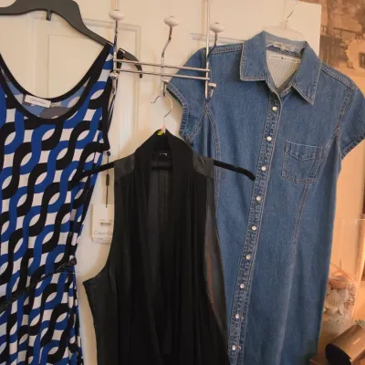 Sale Photo Thumbnail #134: Selection of women's clothing hanging on an over-the-door rack, including a Calvin Klein patterned dress with tags, a black open-front vest, and a Tommy Hilfiger short-sleeve denim shirt dress.