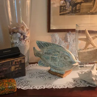 Sale Photo Thumbnail #129: Collection of coastal decor including a carved stone fish figure, glass vases filled with sand, sea shells, and starfish, alongside a small decorative jewelry chest and a Burberry eyeglass case.