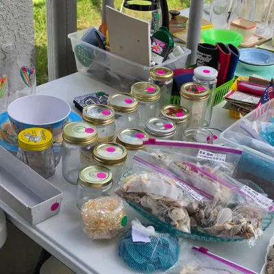 Sale Photo Thumbnail #325: Table assortment of household items, including glassware, mason jars, plastic containers, and craft supplies like bagged seashells.