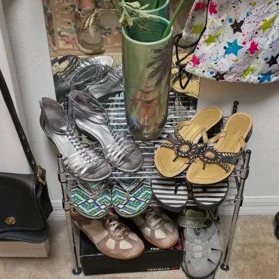Sale Photo Thumbnail #155: Collection of women's shoes displayed on a wire rack, including silver strappy sandals, gold flip-flops, sneakers, and a vintage black Coach leather purse hanging nearby.