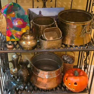 Sale Photo Thumbnail #59: Collection of decorative household items displayed on a metal baker's rack, including brass and copper planters, a jack-o'-lantern, small metallic vases, and a colorful wicker basket.
