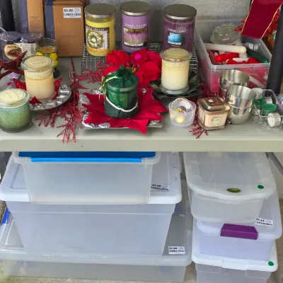 Sale Photo Thumbnail #327: Collection of assorted scented candles, holiday decorations, and plastic storage bins on a folding table.