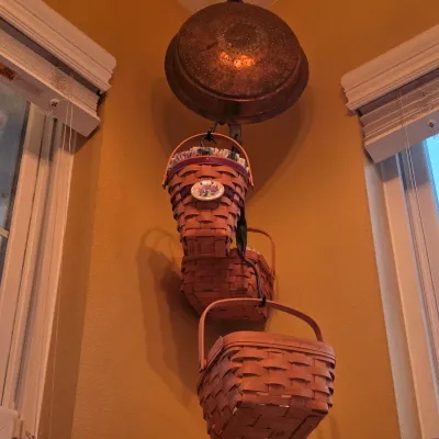 Sale Photo Thumbnail #47: Tiered hanging display of woven Longaberger-style baskets suspended from a vintage copper strainer or bowl in a room corner.