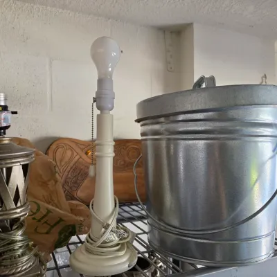 Sale Photo Thumbnail #297: Galvanized metal ash bucket with lid alongside a cream-colored candlestick table lamp and a metal harp-less lamp base.