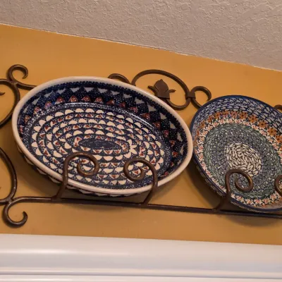 Sale Photo Thumbnail #48: Two pieces of patterned Polish pottery displayed on a wrought iron scrollwork wall rack.