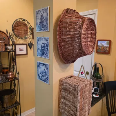 Sale Photo Thumbnail #54: Collection of home decor including wall-mounted wicker baskets, framed Dutch Delft blue tile prints, and a wrought-iron baker's rack filled with various metal and glass items.