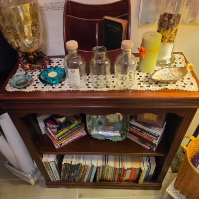 Sale Photo Thumbnail #245: Small wooden bookcase filled with books and topped with decorative items, including glass bottles, candles, and a large metal goblet.