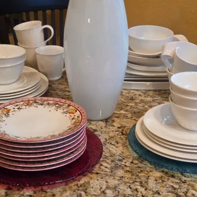 Sale Photo Thumbnail #52: Collection of modern white ceramic dinnerware, mugs, and a tall vase alongside stacked holiday pattern salad plates on glass chargers.