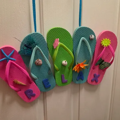 Sale Photo Thumbnail #271: Handcrafted flip-flop door sign spelling out 'RELAX', decorated with beach-themed accents, seashells, flowers, and butterflies.