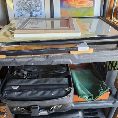 Sale Photo Thumbnail #306: Selection of picture frames in various sizes stacked on a plastic utility shelf, alongside a soft-sided black travel case and home decor items.