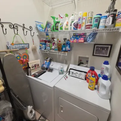 Sale Photo Thumbnail #261: Laundry room set with white top-load washer and dryer, accompanied by shelves stocked with cleaning supplies, laundry detergents, and household accessories.