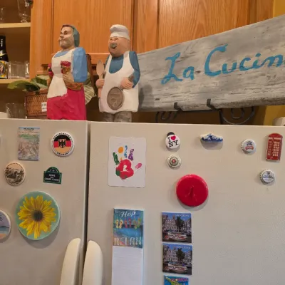 Sale Photo Thumbnail #60: Hand-carved wooden chef and maid figurines displayed alongside a painted wooden "La Cucina" kitchen sign atop a refrigerator.