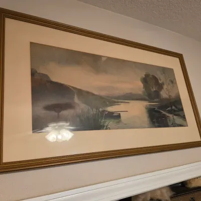 Sale Photo Thumbnail #203: Large framed landscape print depicting a serene river scene with a rowboat, housed in a traditional gilt wooden frame.