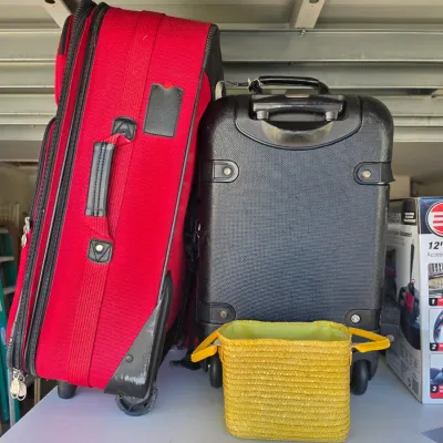Sale Photo Thumbnail #312: Two rolling suitcases, one red soft-side and one black hardshell, paired with a small yellow woven basket tote.