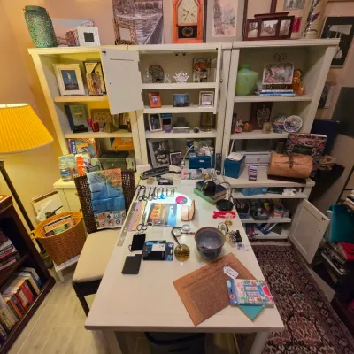 Sale Photo Thumbnail #234: White office desk and matching shelving unit filled with books, small decorative items, craft supplies, and framed art.
