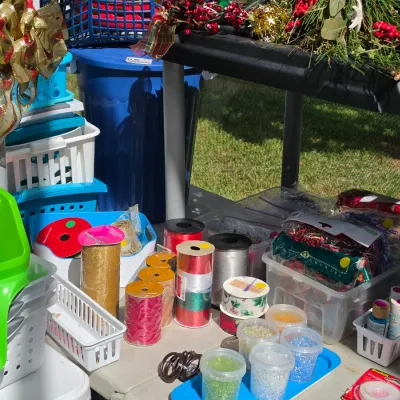 Sale Photo Thumbnail #336: Collection of crafting and holiday supplies including rolls of ribbon, small paint bottles, beads in containers, plastic storage bins, and decorative faux greenery.