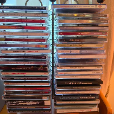 Sale Photo Thumbnail #113: Double-sided metal rack filled with a variety of music CDs in jewel cases, including holiday, pop, country, and compilation albums.