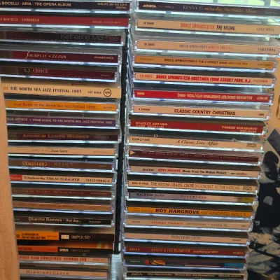 Sale Photo Thumbnail #122: Two stacks of assorted music CDs in jewel cases, featuring titles by artists such as Bruce Springsteen, Andrea Bocelli, and Kenny G.