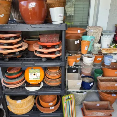 Sale Photo Thumbnail #345: Assortment of garden supplies and planters, including terracotta pots, ceramic planters, rolling plant caddies, and plastic saucer trays arranged on plastic and metal shelving units.