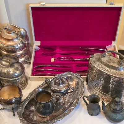 Sale Photo Thumbnail #61: Collection of vintage silver-plated hollowware, including carved metal tiffin lunch boxes, a tea set on a tray, small teapots, and a boxed carving set lined with velvet.