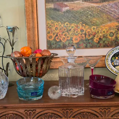 Sale Photo Thumbnail #72: Collection of glassware and decor including Marquis by Waterford crystal decanters, Villeroy & Boch colored glass bowls, cocktail glasses, and a ceramic pitcher displayed on a wooden table.