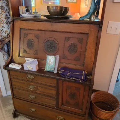 Sale Photo Thumbnail #136: Antique wooden slant-front secretary desk featuring carved floral and medallion panels, brass drawer pulls, and a lower cabinet door.