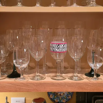 Sale Photo Thumbnail #25: Collection of assorted clear and decorative glassware, including wine goblets and stemmed glasses, displayed on a wooden cabinet shelf.
