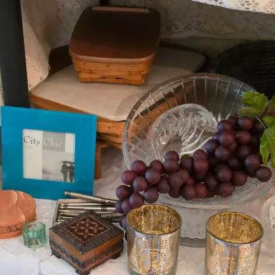 Sale Photo Thumbnail #82: Collection of decorative tabletop accents including a blue picture frame, small carved wooden boxes, gold-tone votive holders, artificial grapes, and clear cut glass bowls.