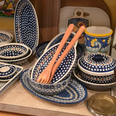 Sale Photo Thumbnail #36: Collection of Polish pottery dinnerware featuring classic blue peacock eye and geometric patterns, including serving bowls, platters, and a covered baker.