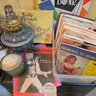 Sale Photo Thumbnail #210: Collection of vintage media and home decor, including 45 RPM records, an oil lamp with clear glass chimney, vintage magazines featuring Elvis, and vintage candy box art.