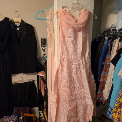 Sale Photo Thumbnail #202: Collection of women's vintage and formal clothing including a pink lace gown, a black Cachet evening dress, and various hanging garments.