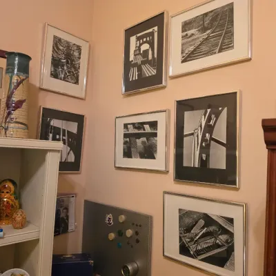Sale Photo Thumbnail #223: Collection of framed black-and-white architectural photographs displayed on a wall alongside decorative objects, including a tall glazed vase, nesting dolls, and globes.