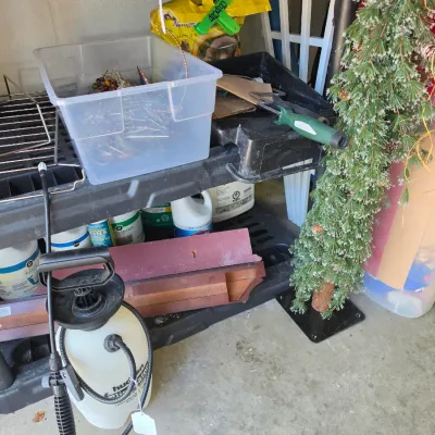 Sale Photo Thumbnail #275: Black plastic utility shelving unit filled with garden supplies, pump sprayer, clear storage tub, and artificial frosted mini pine tree.