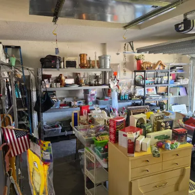 Sale Photo Thumbnail #272: Garage sale setup featuring mid-century style wooden dressers, metal shelving units, holiday decor, framed artwork, and various household goods.