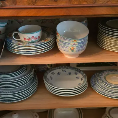 Sale Photo Thumbnail #98: Collection of Villeroy & Boch porcelain dinnerware displayed inside a wooden cabinet, including tulip-patterned cups, plates, and patterned bowls.