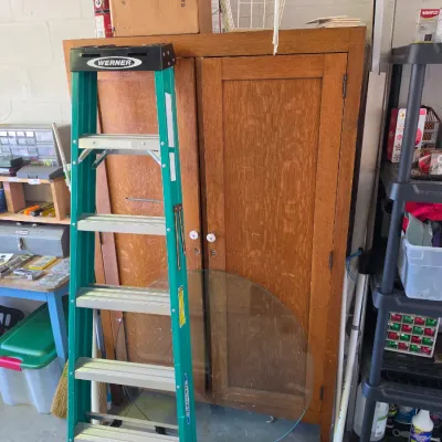 Sale Photo Thumbnail #281: Green Werner fiberglass step ladder positioned in front of a vintage wooden double-door storage cabinet in a garage setup.
