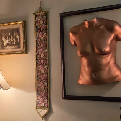 Sale Photo Thumbnail #128: Collection of wall decor including a framed metallic female torso sculpture, a vintage needlepoint bell pull, and a framed black-and-white family portrait.