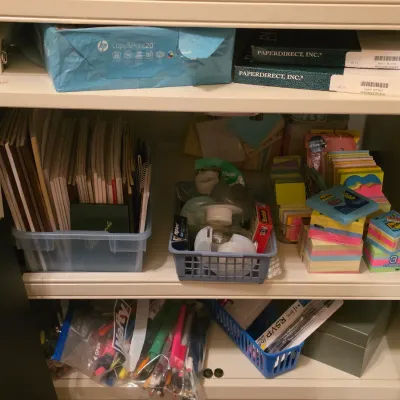 Sale Photo Thumbnail #230: Cabinet filled with an assortment of office supplies including printer paper, spiral notebooks, sticky note pads, tape dispensers, and writing utensils in plastic organizers.