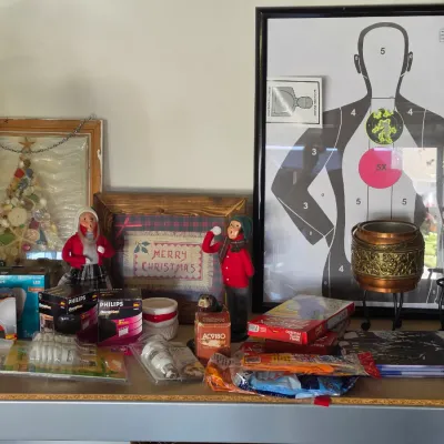 Sale Photo Thumbnail #294: Collection of shelf items including framed Christmas decor, vintage knee-hugger elves, light bulbs, a framed shooting target, and an ornate brass pot.
