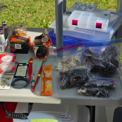 Sale Photo Thumbnail #337: Assortment of crafting supplies laid out on a table, including hot glue items, craft paints, clear plastic organizers, and bagged pinecones.