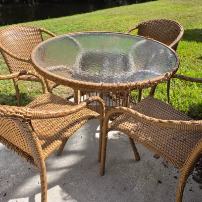 Sale Photo Thumbnail #342: Outdoor patio dining set featuring a round glass-top table with a woven rim and four matching brown resin wicker armchairs.