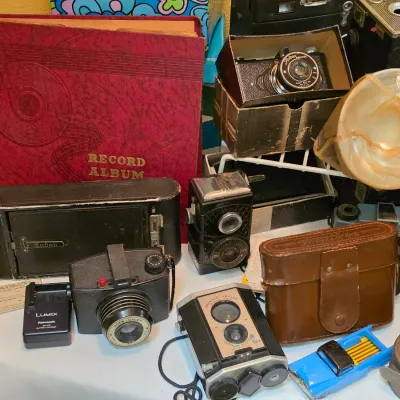 Sale Photo Thumbnail #206: Collection of vintage cameras, accessories, and a red record album, including a Kodak folding camera, Brownie Reflex, and a leather camera case.