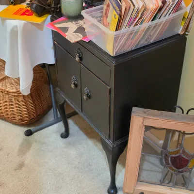 Sale Photo Thumbnail #212: Black painted Queen Anne style side cabinet with cabriole legs, featuring metal hardware, surrounded by vintage books, baskets, and a stained glass panel.