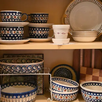 Sale Photo Thumbnail #38: Collection of Polish pottery ceramics inside a wooden cabinet, featuring cups, saucers, and serving bowls with classic peacock eye and geometric patterns.