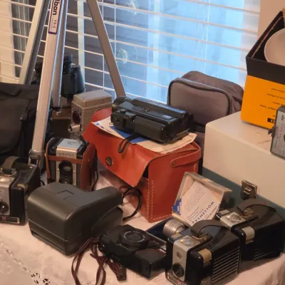 Sale Photo Thumbnail #176: Collection of vintage cameras, equipment, and accessories including a Velbon VS-3 tripod, Kodak Brownie box cameras, Argoflex TLR, a Polaroid instant camera, and carrying cases.
