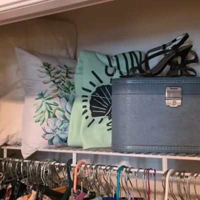 Sale Photo Thumbnail #201: Vintage blue Emerald train case, black strappy high heel sandals, throw pillows, and folded clothing resting on a wire closet shelf.