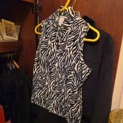 Sale Photo Thumbnail #257: Black and white zebra print fleece vest by Charter Club hanging on a yellow plastic hanger alongside dark outerwear in a closet.
