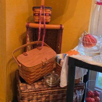 Sale Photo Thumbnail #46: Collection of woven baskets, including a Peterboro-style picnic basket with a wooden lid, alongside decorative glassware and fall accents.