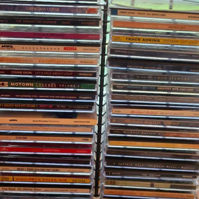 Sale Photo Thumbnail #123: Vertical metal wire CD rack filled with a collection of compact discs in jewel cases from various pop, country, and holiday artists from the 1990s and 2000s.